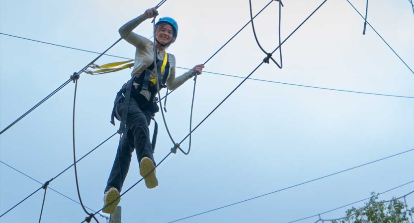 A person wearing safety gear is secured by ropes as they navigate a high ropes course. 